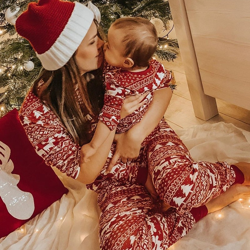 une maman et un bébé en pyjama de noel assortis devant leur sapin de noel