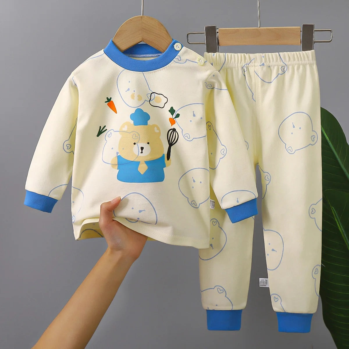 Pyjama Ourson pour Bébé/Enfant beige avec le bout des manches et du col en bleu, un ourson habillé en tenue bleu de cuisine avec un fouet de cuisine dans les main au centre du haut de pyjama et des motifs d'ourson  qui se fondent sur le pyjama sur le reste du pyjama 