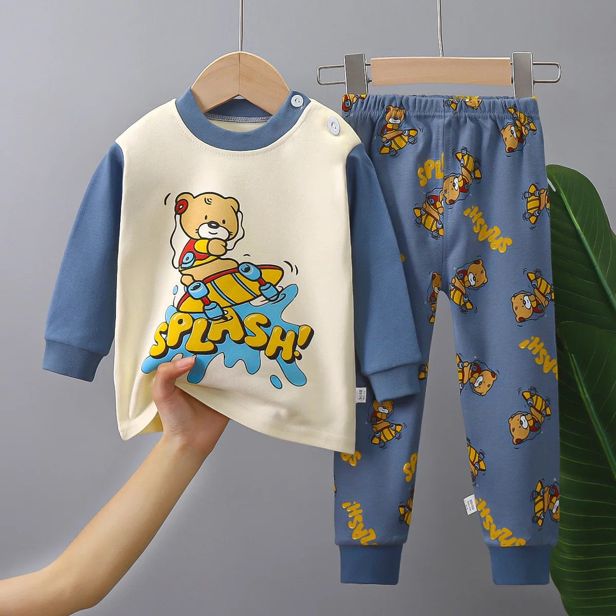 Pyjama Ourson pour Bébé/Enfant composé d'un haut beige avec les manches et le col bleu et au centre un motif d'ourson qui fait du skate avec une écriture jaune "splash !", et d'un pantalon bleu avec plusieurs petits motifs d'ourson qui font du skate et des motifs d'écriture jaune "splash"