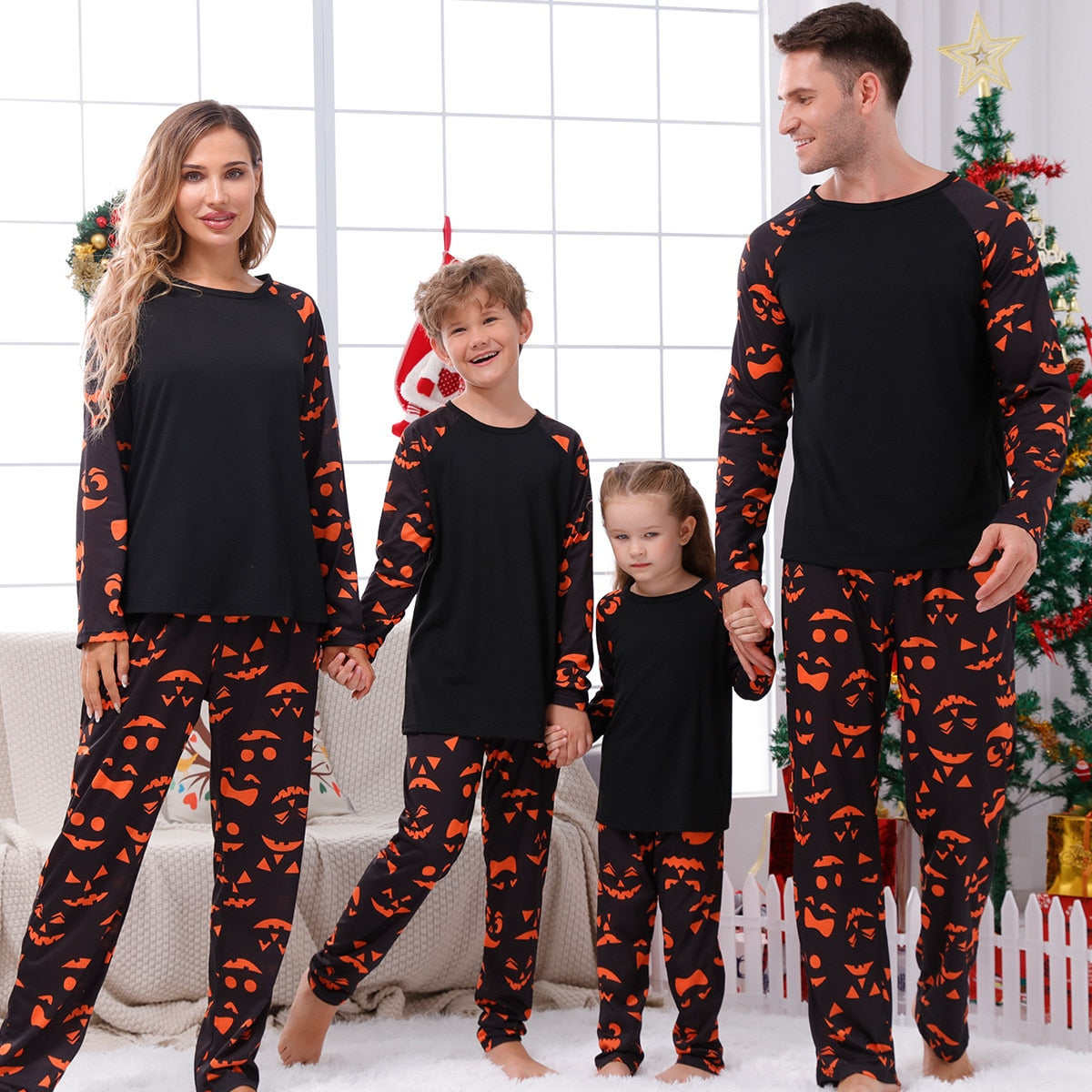 famille composé du père de la mère du fils et de la fille qui pose en portant un pyjama d'halloween assorti de couleur noir avec des visage de citrouilles d'halloween orange 